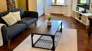 Un salon avec un canapé, une table basse, un téléviseur et une fenêtre avec des rideaux.