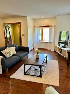 Un salon avec un canapé, une table basse, un téléviseur et une fenêtre avec des rideaux.