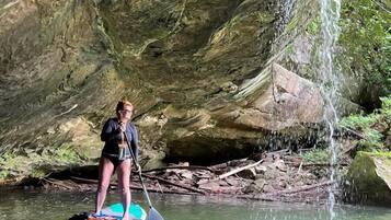 A person paddleboarding in a natural setting with a waterfall and rocky cliffs.