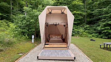 Tienda de campaña con cama en su interior, rodeada de un bosque.
