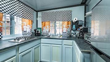 A kitchen with checkered curtains, a gas stove, a sink, and a coffee machine.