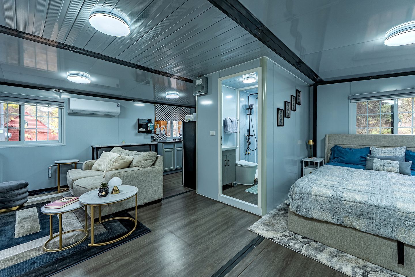 A modern bedroom with a large bed, a seating area with a sofa and coffee table, a walk-in closet, and a bathroom with a shower and toilet.