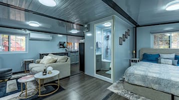 A modern bedroom with a large bed, a seating area with a sofa and coffee table, a walk-in closet, and a bathroom with a shower and toilet.