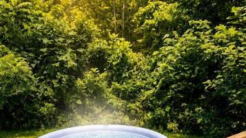 A hot tub on a wooden deck surrounded by lush greenery.