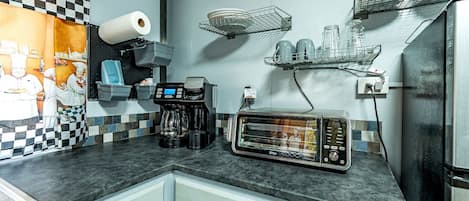 Una cocina con cafetera, tostadora y estantes con vajilla.