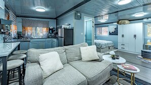 Een moderne keuken met een geruit spatwand, een bank met kussens, een eethoek met barstoelen en een kleine ronde tafel met een boek en een plant.