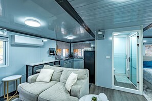 Een ruimtelijk ingerichte leefruimte met een kitchenette, een sofa en een glazen deur naar buiten.