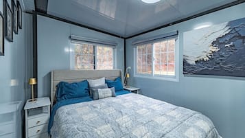 Une chambre à coucher avec un lit, deux fenêtres, une table de chevet et une lampe fixée au mur.