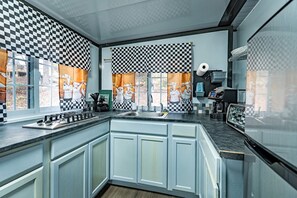 Een keuken met geruit gordijnen, een gasfornuis, een gootsteen en een koffieapparaat.