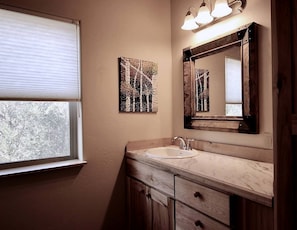 Un baño con ventana, lavamanos, espejo y decoración en la pared.