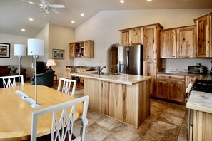 A modern kitchen with wooden cabinets, a central island, stainless steel appliances, and a dining area with a white table and chairs.