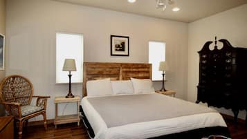 Un dormitorio con cabecera de madera, dos lámparas de noche, una silla de mimbre, un aparador y un ventilador de techo.