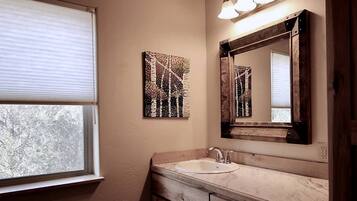 Un baño con ventana, lavamanos, espejo y decoración en la pared.