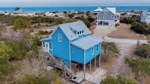 Une maison située sur la côte, avec une façade bleue très visible, une terrasse et une vue sur l’océan.