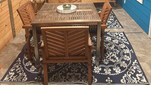 Une table à manger en bois, des chaises, un banc avec des coussins et un tapis à motifs sur un sol carrelé.