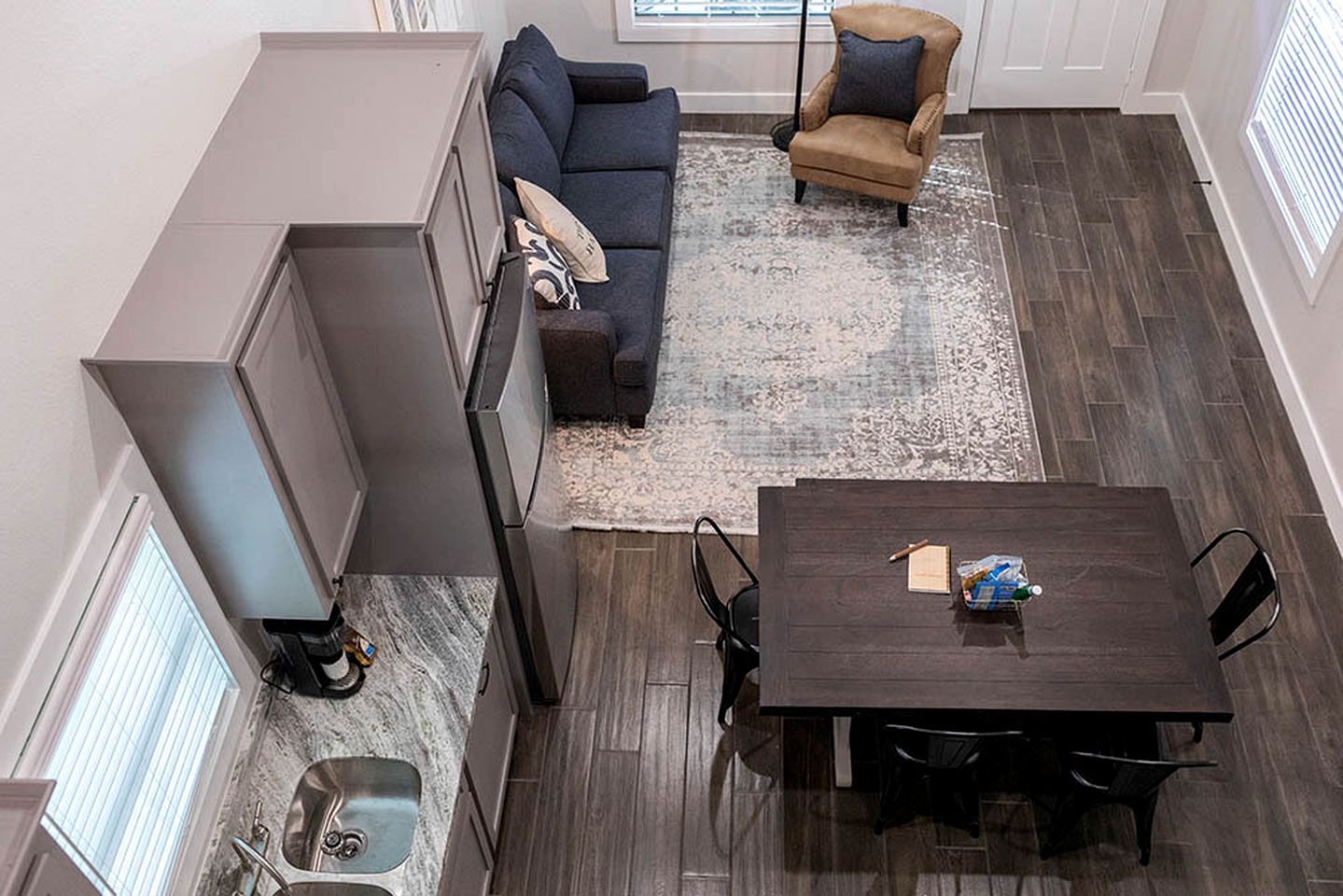 A compact living space with a dark wood floor, a dark wood dining table, a sofa, a chair, and a small kitchen area with a sink.