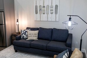 Un soggiorno moderno con un divano grigio scuro, una lampada a sospensione geometrica e un’opera d’arte appesa sopra il divano.