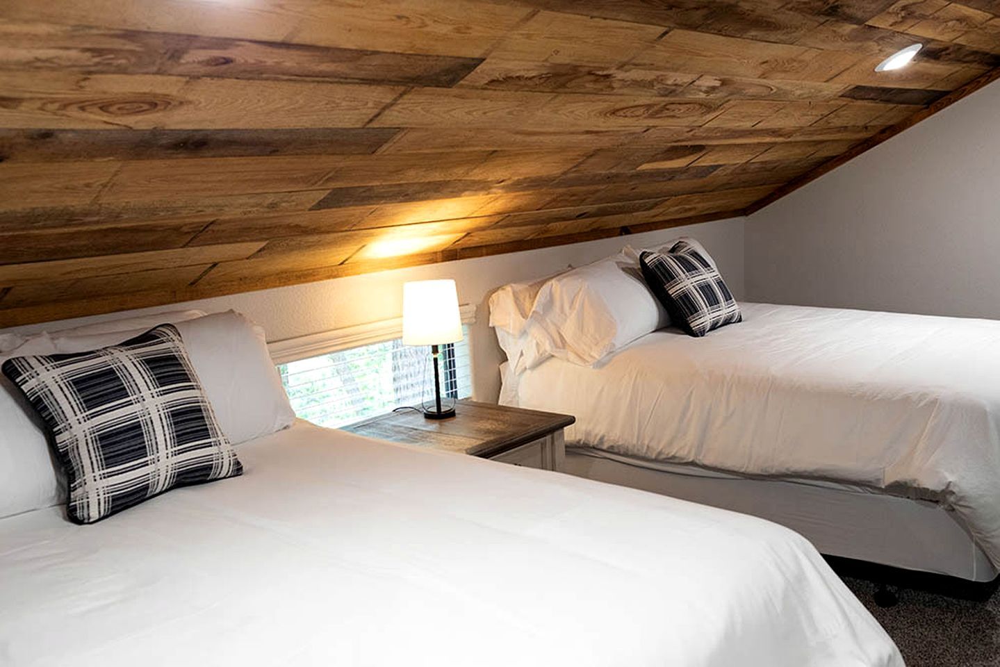 Ein Zimmer mit zwei Betten, einem Nachttisch mit Lampe und einer Holzbalkendecke.