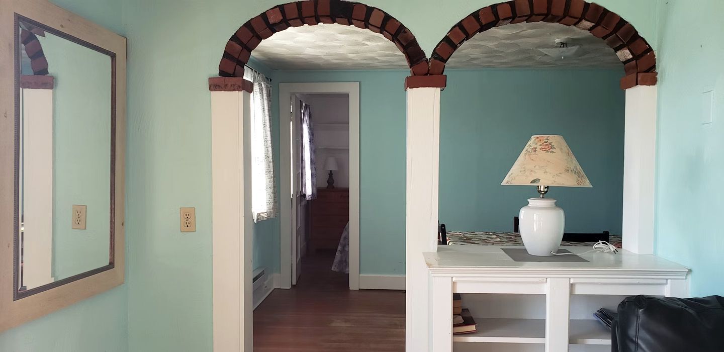 A hallway with a mirror, a lamp, and a staircase leading to another room.