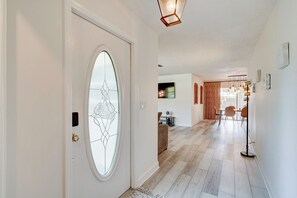 Un couloir avec une porte blanche, une fenêtre en verre décoré, un coin repas avec des chaises et une table, et un lampadaire.