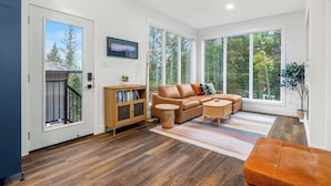 A modern living room with a leather sofa, wooden side table, and a large window with a view of trees.
