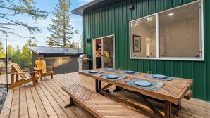 A wooden deck with a dining table set for six, outdoor chairs, and a grill area.