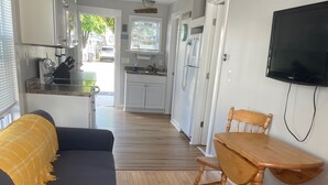 Un espacio habitable compacto con sofá, mesa de comedor, sillas, zona de cocina y televisor.