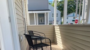 Un espacio al aire libre cubierto con una terraza de madera, dos sillas de metal y una señal de stop al fondo.