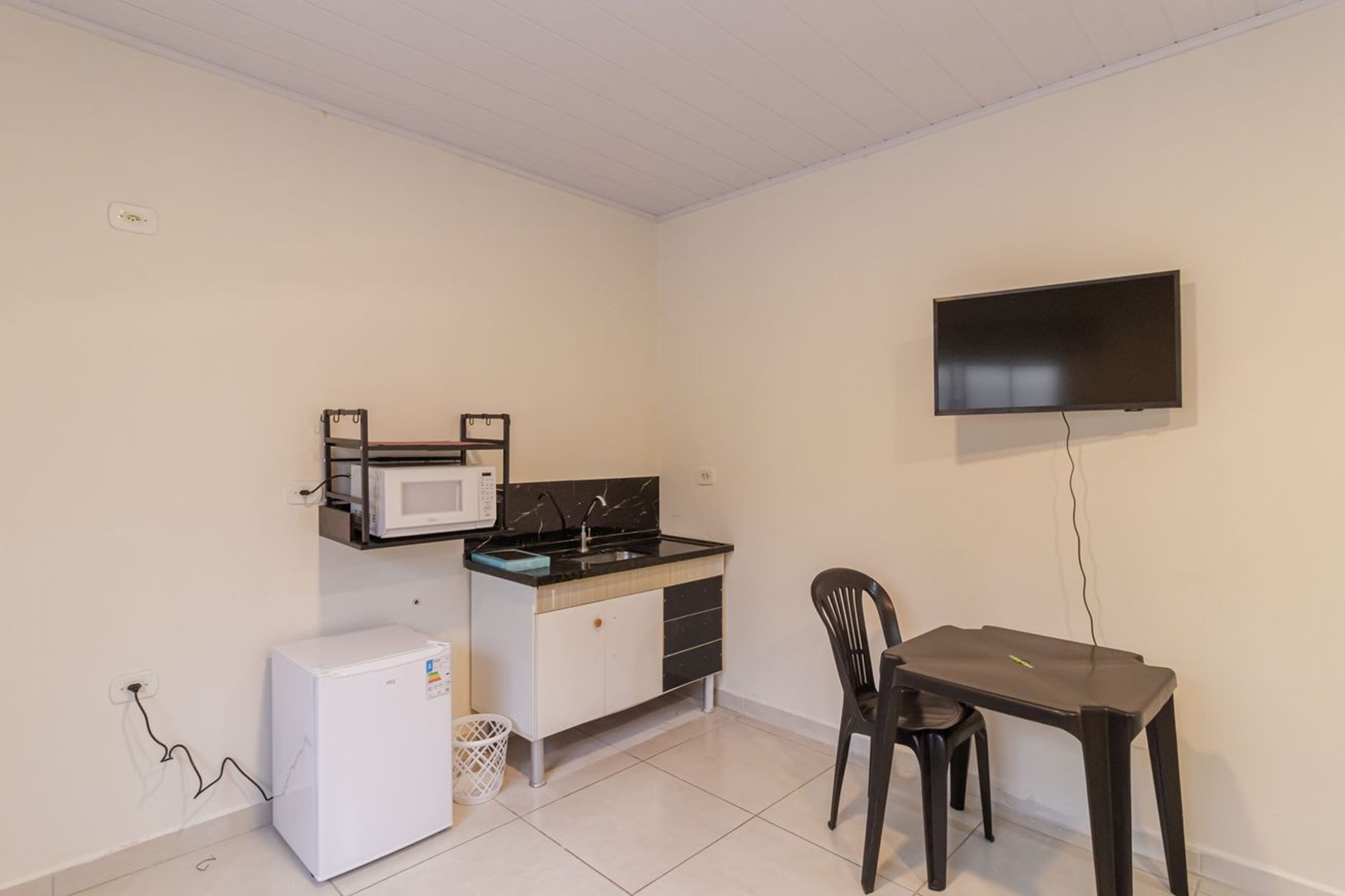 Une petite cuisine équipée d’un four à micro-ondes, d’une cuisinière et d’un réfrigérateur, une table à manger avec une chaise, et un téléviseur fixé au mur.