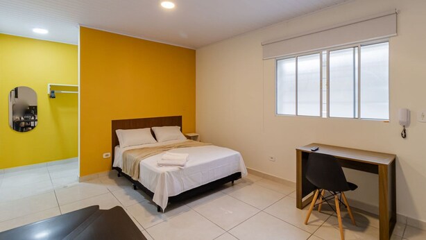Une chambre d’hôtel avec un lit, un bureau, une chaise, une fenêtre et un miroir.