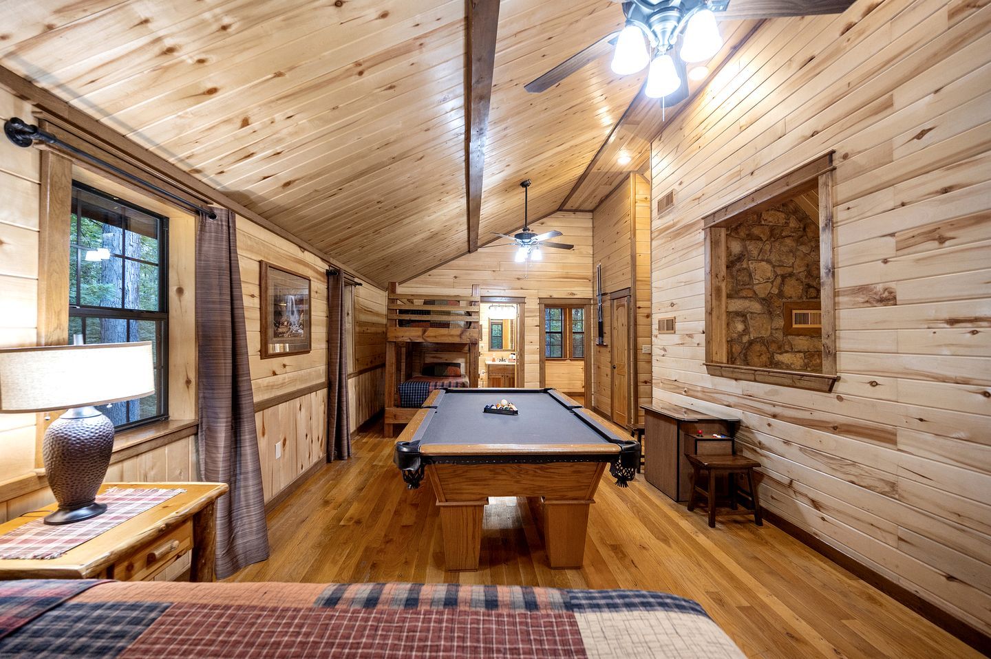 A wooden cabin interior with a pool table, a ceiling fan, and a bunk bed.