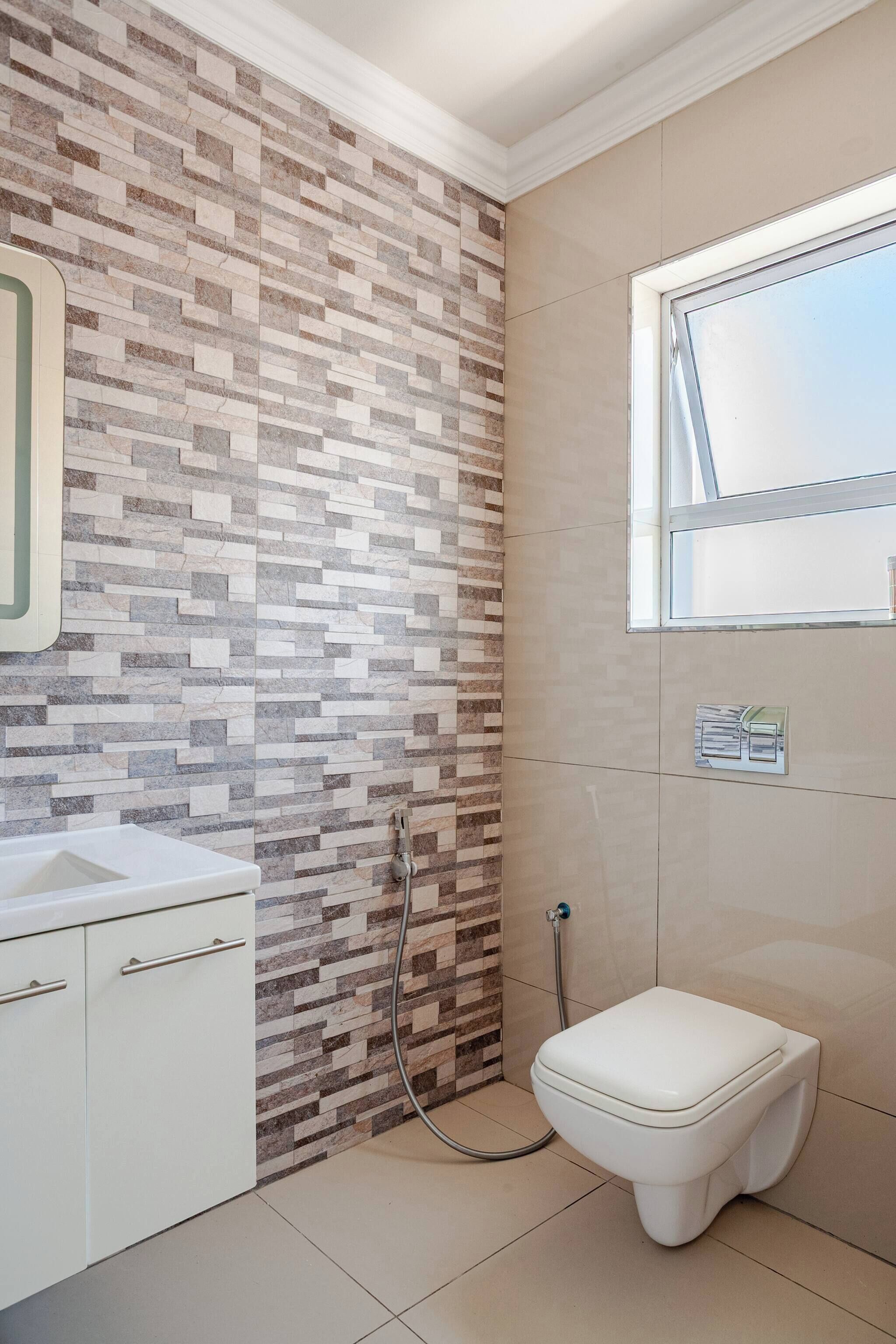 Une salle de bain avec un mur carrelé, une fenêtre, des toilettes et un lavabo.