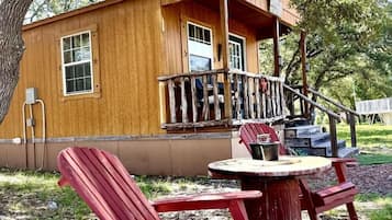 Una cabaña de madera con un porche, sillas Adirondack rojas y una mesa.