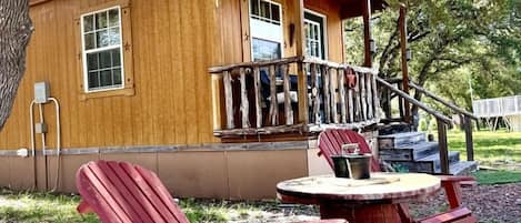 Eine Holzhütte mit Veranda, roten Adirondack-Stühlen und einem Tisch.