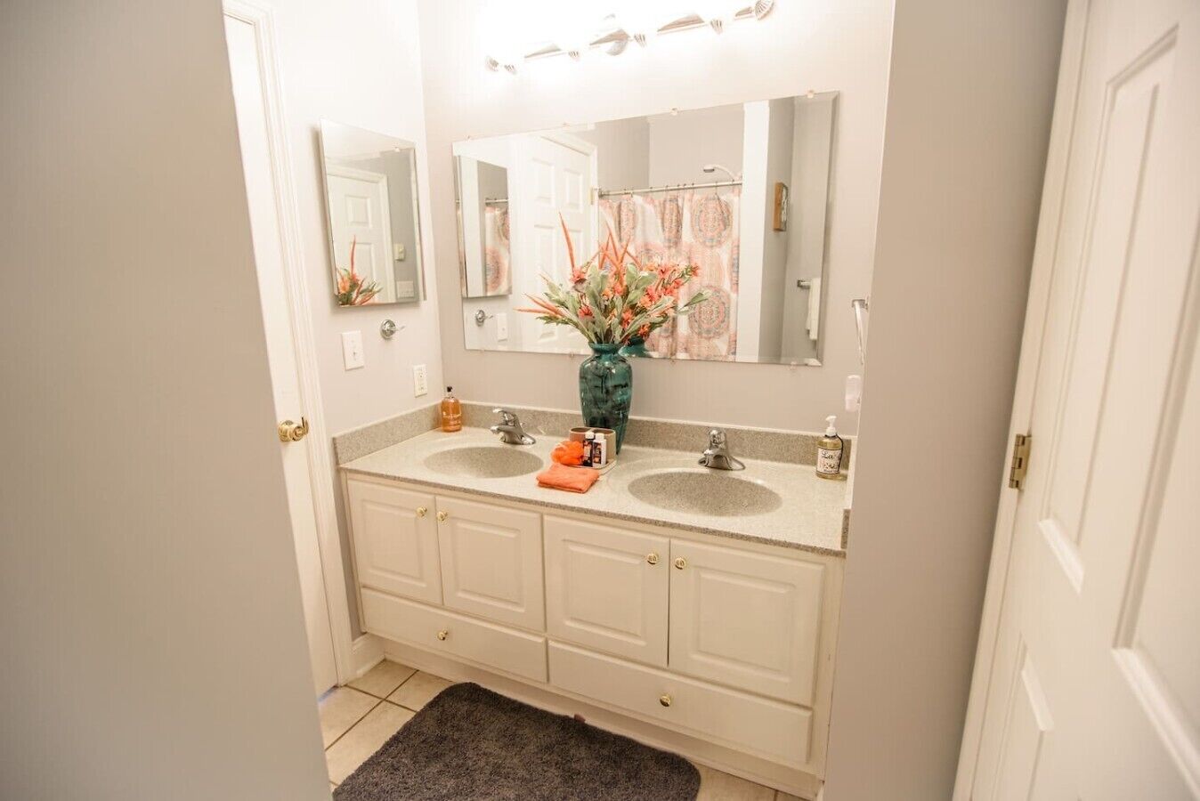 A bathroom with two sinks, a large mirror, and a vase with flowers.