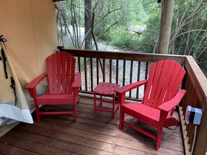 A wooden deck with two red Adirondack chairs and a small table, surrounded by trees.
