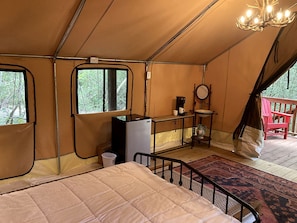 A tented room with a bed, a small table, a chair, and a window.