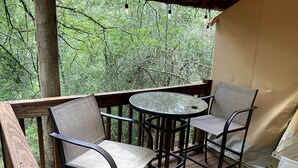 A wooden deck with two chairs and a table, surrounded by trees. - Enjoy a Glamping Experience at this Safari Tent in Livingston, Texas (Livingston)