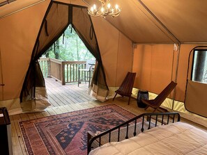 Un hébergement sous tente comprenant un lit, une chaise, un tapis et un balcon.