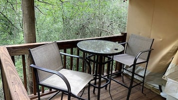 A wooden deck with two chairs and a table, surrounded by trees.