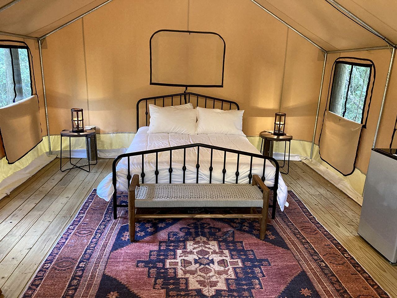A tented room with a bed, a bench, and two nightstands.