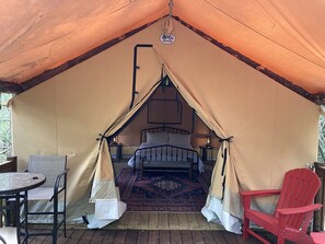 A tented accommodation with a bed, a table, and two chairs.