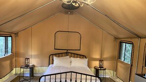 A tented room with a bed, two nightstands, a chandelier, and windows. - Enjoy a Glamping Experience at this Safari Tent in Livingston, Texas (Livingston)