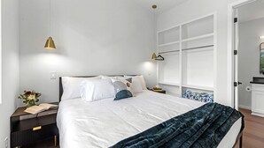 Quarto moderno com cama, mesas de cabeceira, um criado-mudo, uma janela e uma porta.