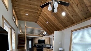 A compact living space with a kitchenette, a sofa, a ceiling fan, and a staircase leading to an upper level.