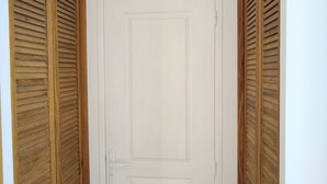 Uma porta branca com design retangular simples, ladeada por painéis de madeira veneziana.