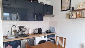 Cuina petita amb armaris foscos, taula de dinar de fusta, rentadora i cafetera.