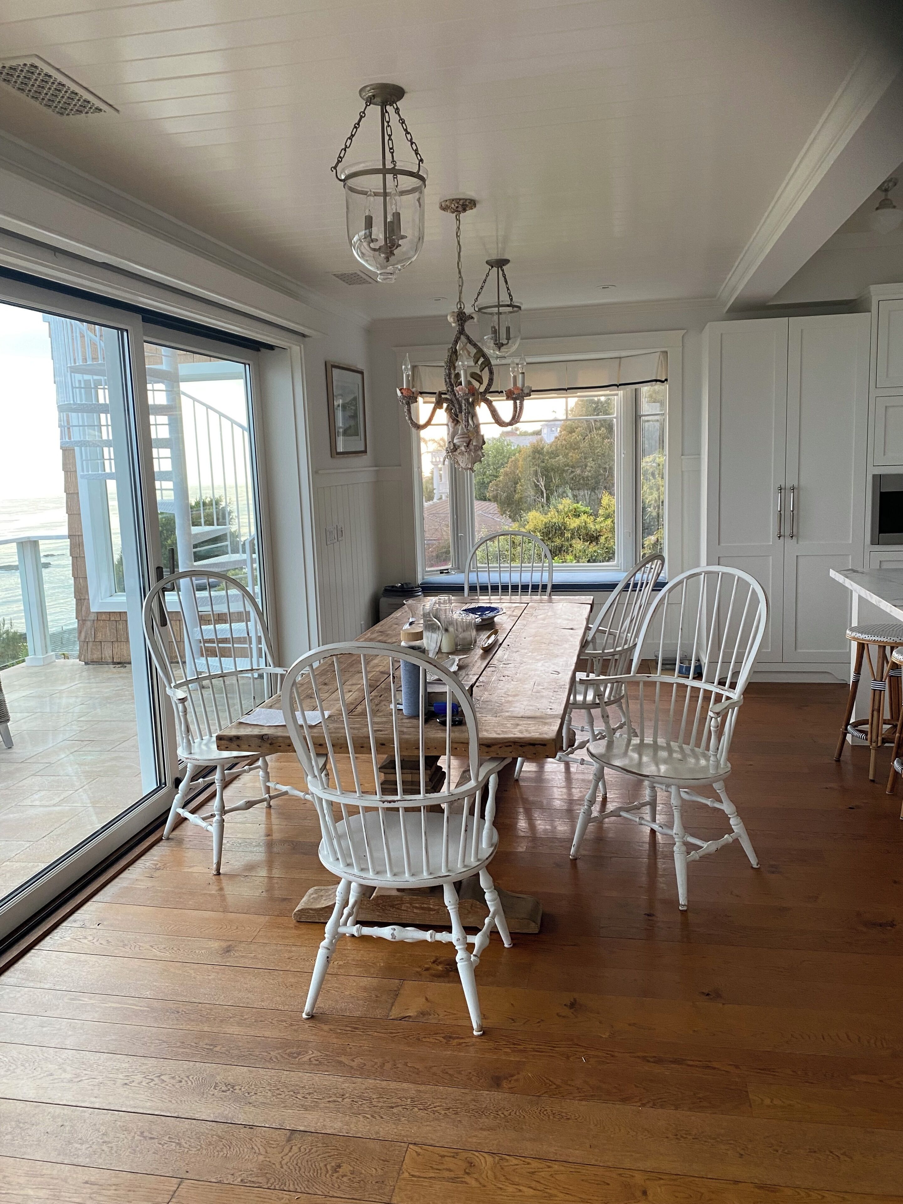 A dining area with a large wooden table, white chairs, and a chandelier.