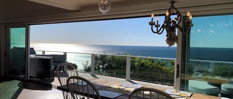 A balcony with a view of the sea, a table with chairs, and a chandelier.