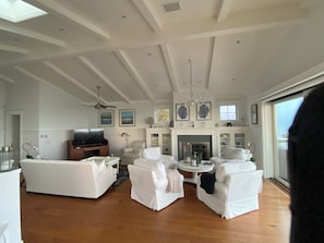 A spacious living room with a fireplace, white furniture, and a large window. - Cape Cod inspired Malibu Beach home (Malibu)
